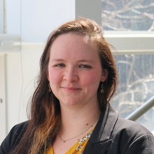 A close-up of Kaity Fisher. She's wearing a dark blazer and standing in front of an outdoor background.