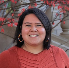 A close-up shot of Taylor Beyal. She's wearing a red blouse and is standing in front of a floral and stone background.